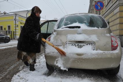 Женщина счищает снег с автомобиля.