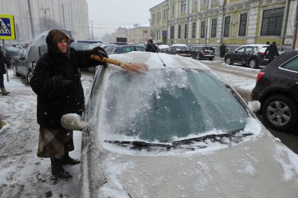 Женщина счищает снег с автомобиля.