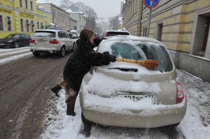 Женщина счищает снег с автомобиля.