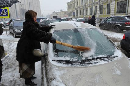 Женщина счищает снег с автомобиля.