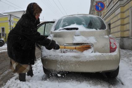 Женщина счищает снег с автомобиля.