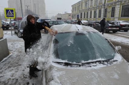 Женщина счищает снег с автомобиля.