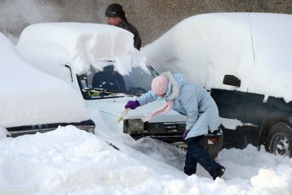 Последствия снегопада. Девушка счищает снег с автомобиля.