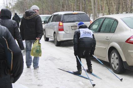 Лыжник едет мимо припаркованных автомобилей.