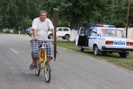 Мужчина с веслом едет на велосипеде мимо автомобиля полиции.