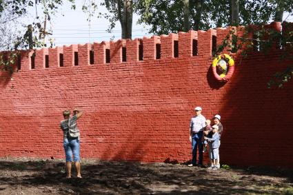 Кирпичная стена напоминающая кремлевскую. Рядом со стеной фотографируются люди.