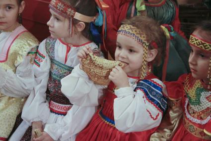 Девочка в национальном костюме ест блин.