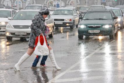 Женщина с ребенком переходят дорогу по лужам.