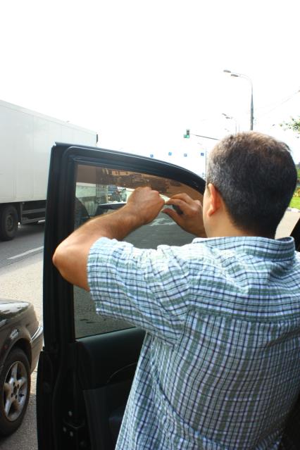 Мужчина снимает тонированную пленку со стекла своего автомобиля.