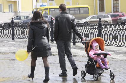 Мужчина и женщина гуляют с ребенком в детской коляске.