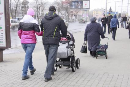 Мужчина и женщина гуляют с ребенком в детской коляске.