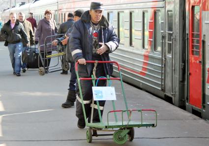 Носильщик с тележкой для багажа проходит по перрону вокзала.