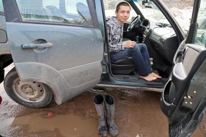 Мужчина сидя в внедорожнике одевает резиновые сапоги.