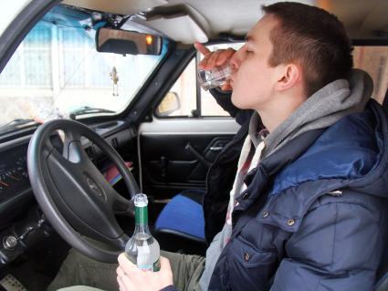 Мужчина за рулем автомобиля пьет водку.