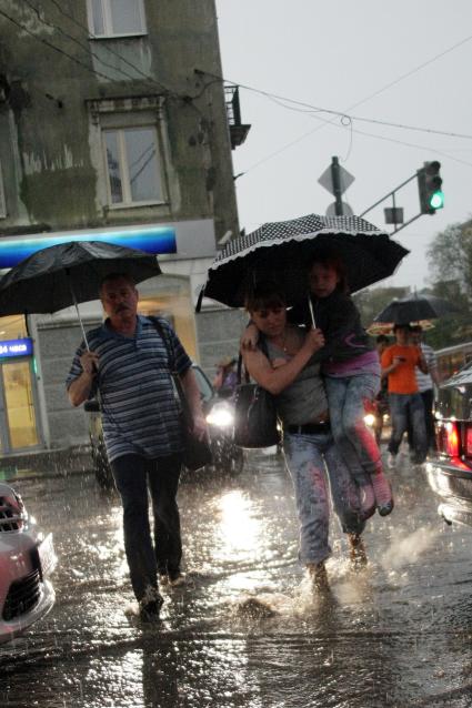 Люди под зонтами идут по затопленной под ливнем улице.