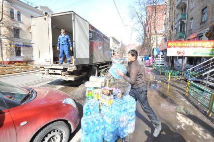 Рабочие выгружают из машины упаковки с водой и напитками. Магазин `Куриный дом` (справа).