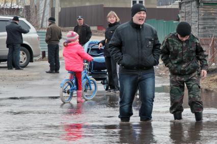 Молодежь идет по затопленной паводком улице по колено в воде.