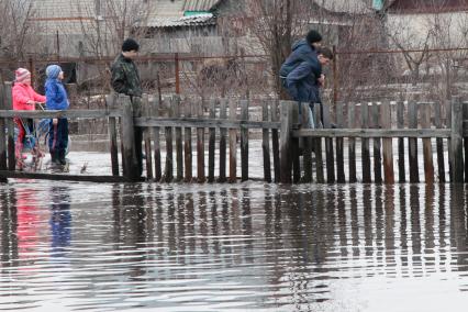 Молодежь идет по затопленной паводком улице по колено в воде.