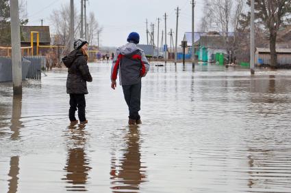 Два ребенка в резиновых сапогах посередине затопленной улицы.