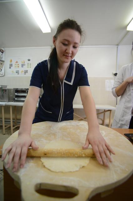 Женщина скалкой раскатывает тесто на разделочной доске.