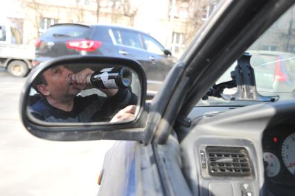 Пьянство за рулем. На снимке: водитель пьет вино в салоне автомобиля.