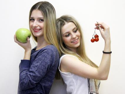 Девушки держат в руках овощи и фрукты.