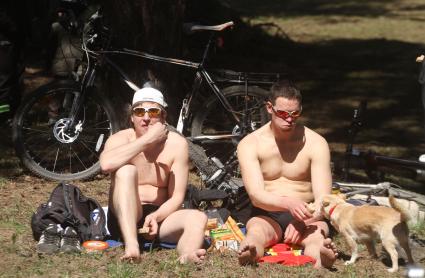 Два парня загорают на солнце, кормят собаку сосиской.
