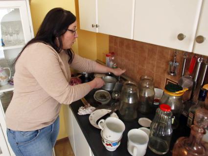 Женщина моет грязную посуду руками.