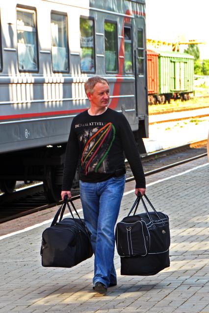 Мужчина с сумками идет по перрону вокзала.