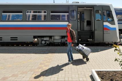 Женщина с сумкой на колесиках выходит из вагона поезда.