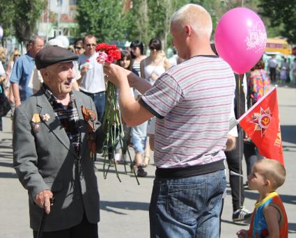 Мужчина с ребенком на 9 мая дарит ветерану гвоздики.