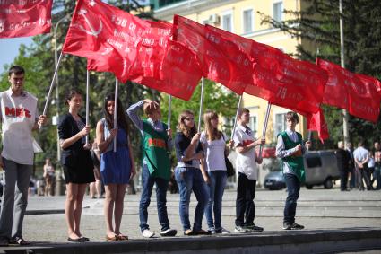 Молодежь держит в руках красные флаги, один парень причесывается рукой