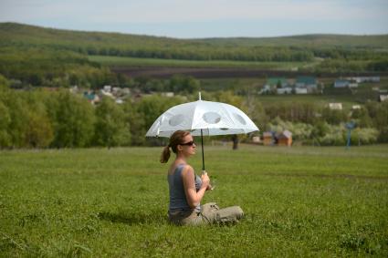 Отдых на природе. На снимке: девушка под зонтиком сидит на поляне.