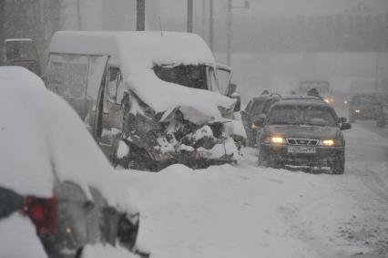 Снегопад в городе. На снимке: аварийный микроавтобус и автомобили на заснеженной дороге.