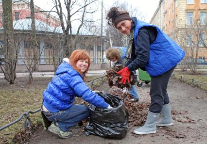 Женщины собирают осеннюю листву в пакеты для мусора.