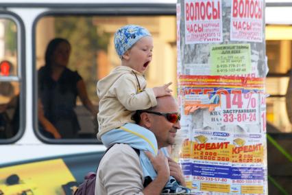 Мужчина несет на плечах зевающего ребенка.