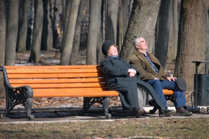 Два пенсионера греются на солнце сидя на лавочке в парке.