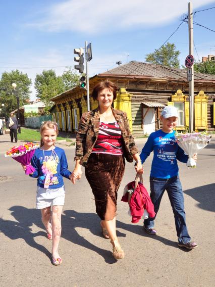 Женщина ведет под руки детей с цветами в школу.