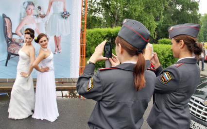 Две девушки полицейские фотографируют двух девушек в свадебных платьях.