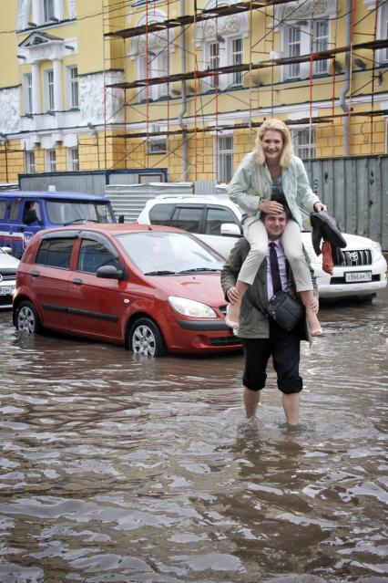 Последствия ливня в городе - затопленные улицы. Мужчина переходит босиком затопленную улицу, несет на плечах девушку.