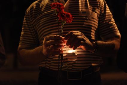 Мужчина держит в руках стаканчик со свечой и гвоздики