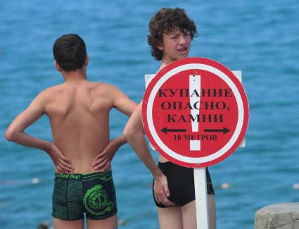 Отдых на море. На снимке: подростки у знака `Купание опасно, камни`