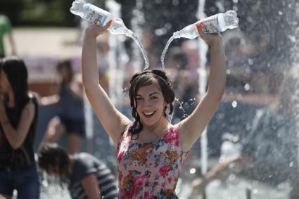 Девушка, стоя в фонтане, льет из двух бутылок воду себе на голову