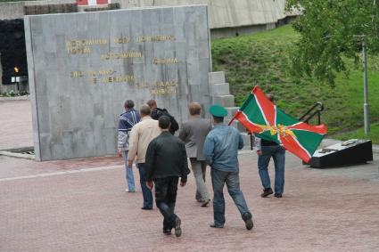 День пограничника. Мужчины с флагом пограничных войск у мемориала.