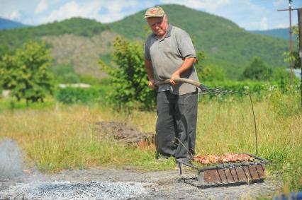 Приготовление шашлыка. На снимке: мужчина держит на вилах мангал с шумпурами