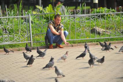 Мужчина кормит голубей на городской улице.