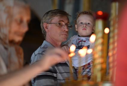 Мужчина с ребенком на руках в церкви у подсвечника.