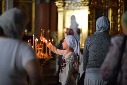 Девочка в церкви ставит свечку в подсвечник.