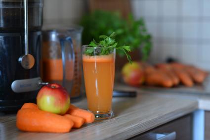 Стакан свежевыжатого морковно-яблочного сока, украшенный веточкой петрушки.