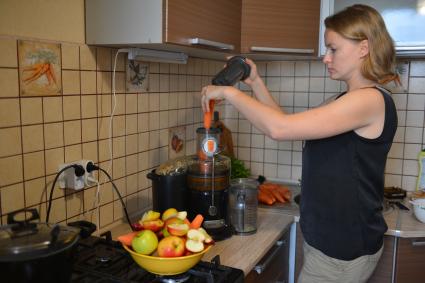Девушка готовит свежевыжатый сок из яблок и моркови.